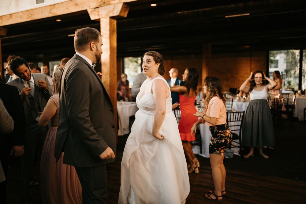 Bride and groom share a joyful moment on the wedding reception dance floor surrounded by celebrating guests.