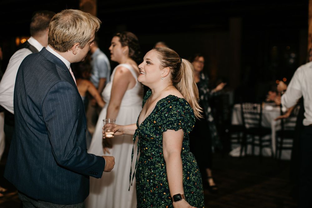 Young woman in floral green dress laughs while conversing with a man at a wedding reception.