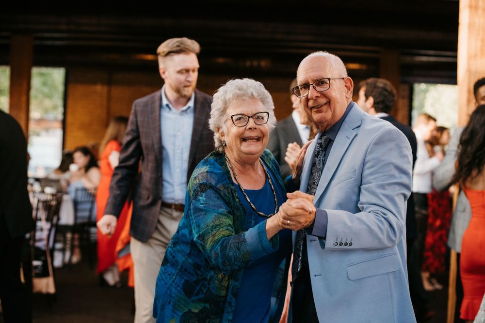 Elderly couple smiling and dancing together at a wedding reception in a rustic venue.
