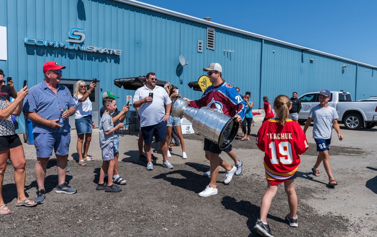 Crowd of people gathered outside a blue industrial building on a sunny day.