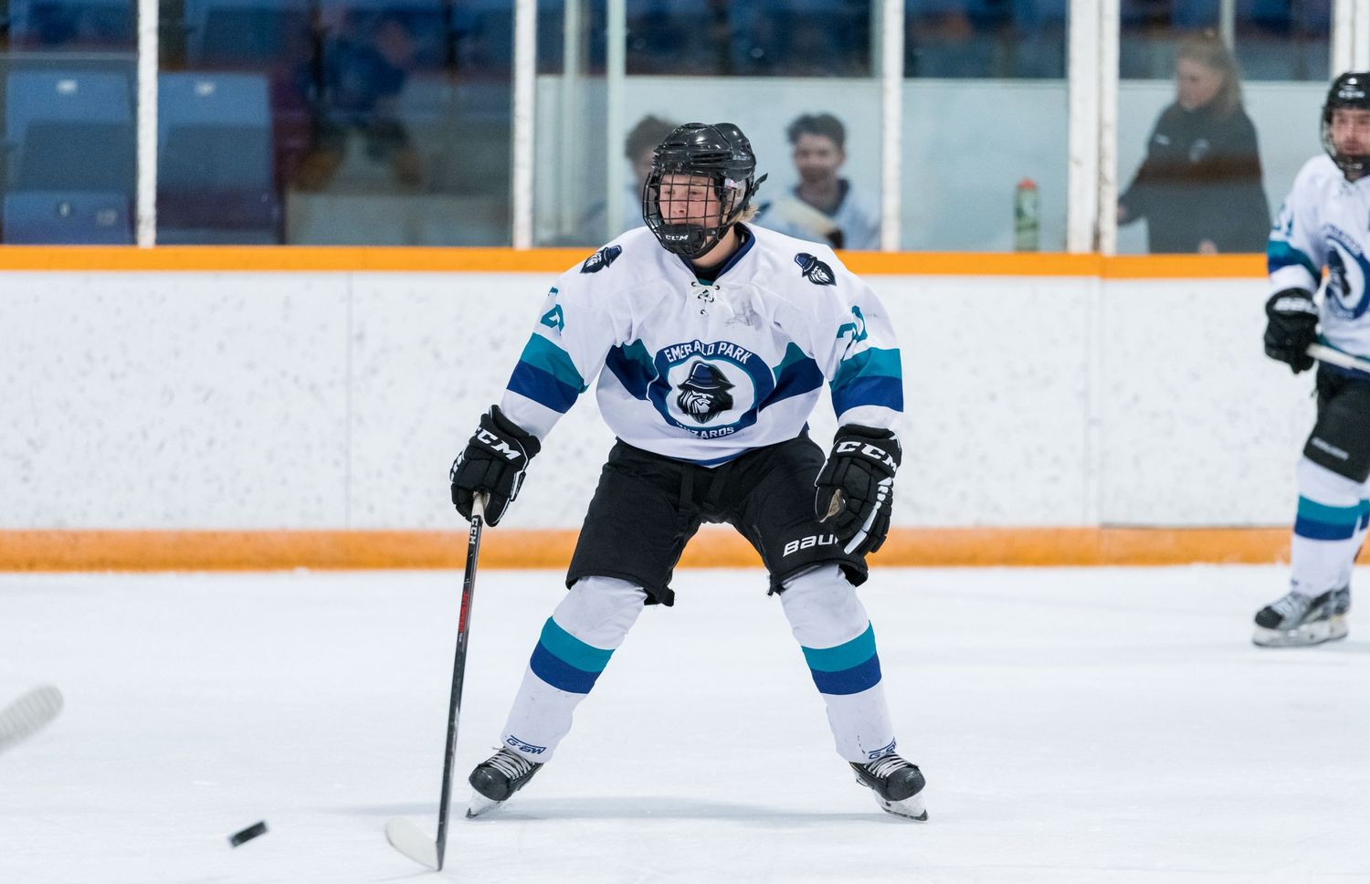 Hockey player in light blue jersey with team logo stands ready during game action.