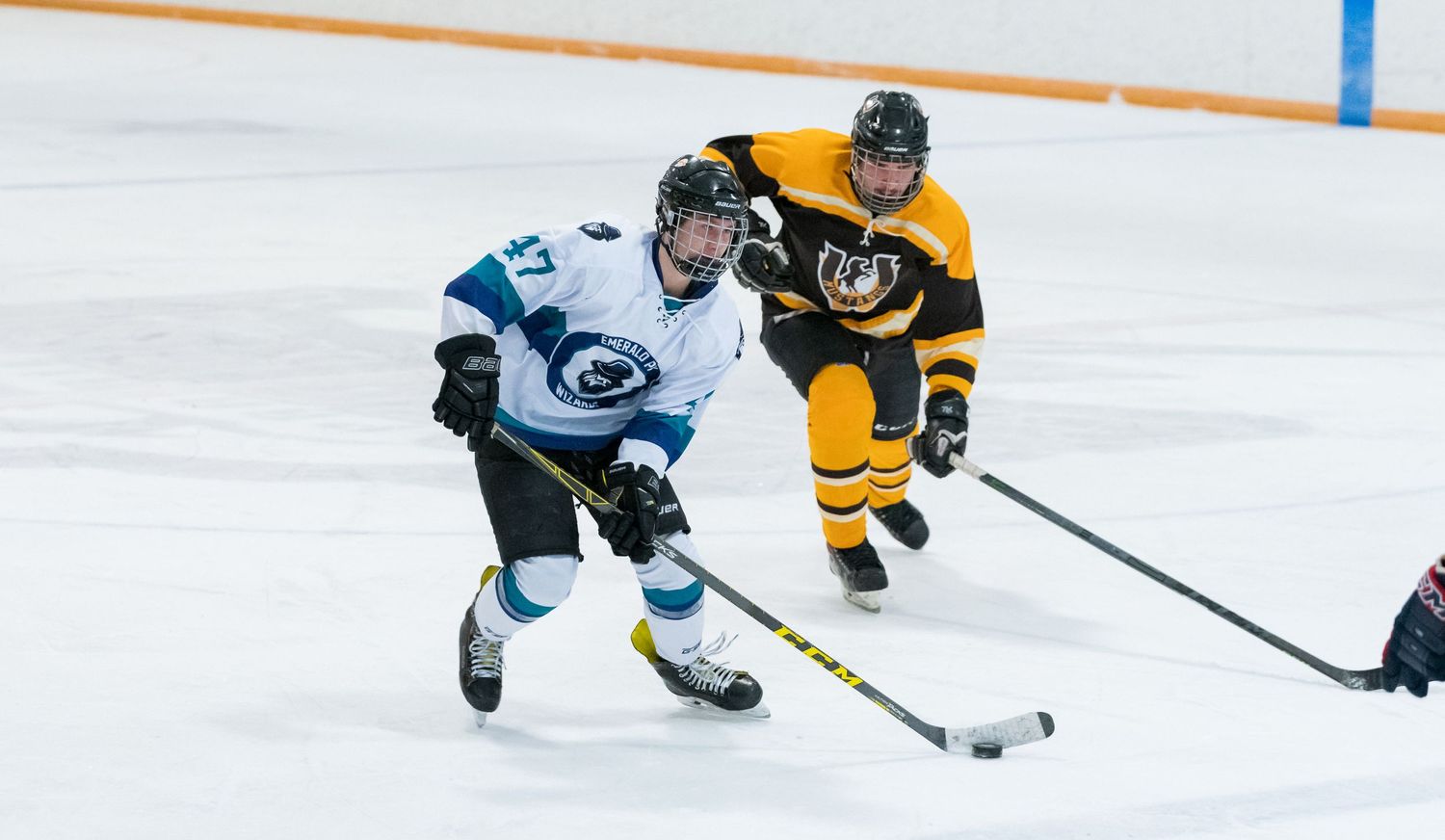 Two hockey players battle for the puck during an intense game with one in yellow and one in light blue uniforms.