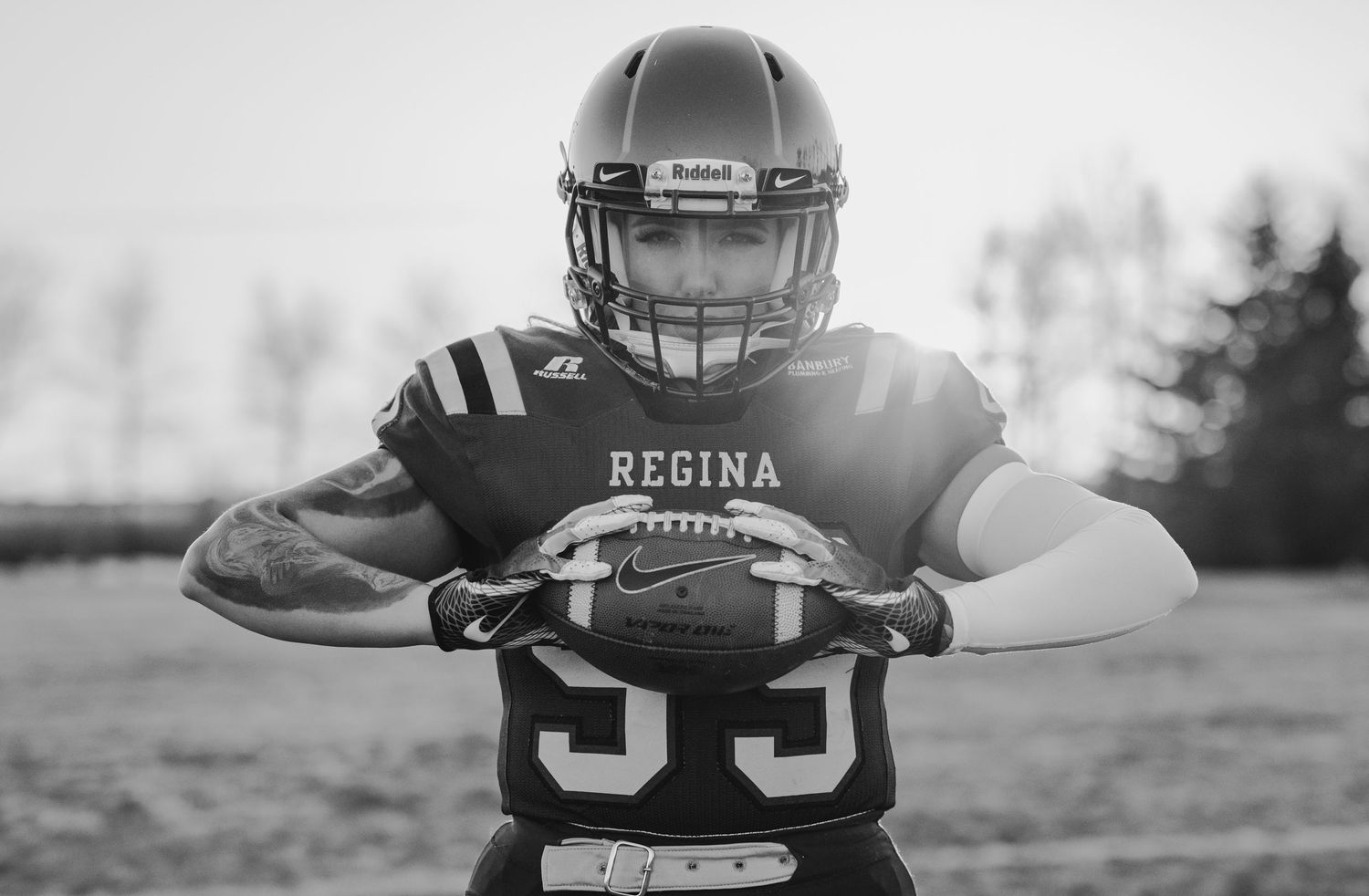 Black and white portrait of Regina football player holding ball in dramatic pose.