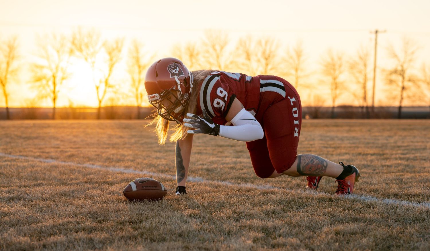 Football player in red Regina uniform does plank position with ball during sunset.