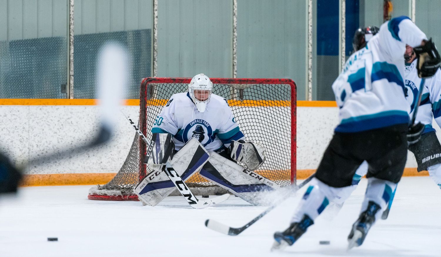 Hockey goalie defends net as players compete during intense ice hockey match.