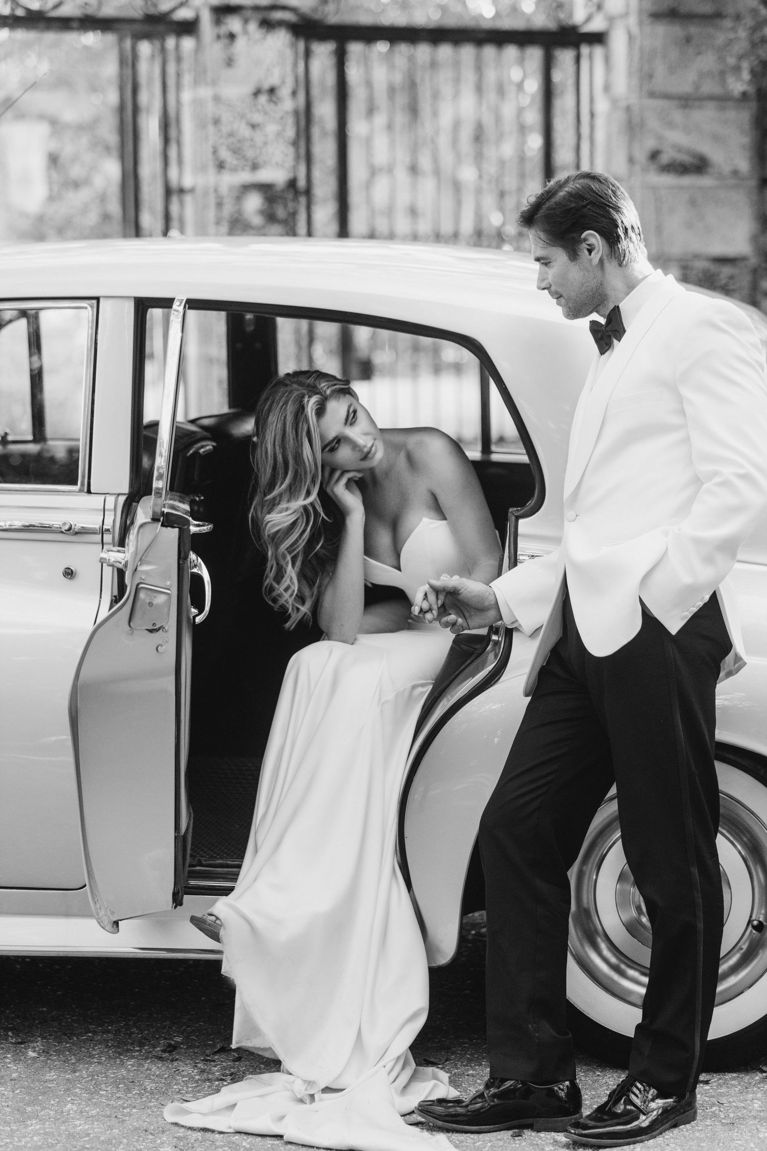 A classic vintage car scene with elegant formal attire and romantic black and white photography.