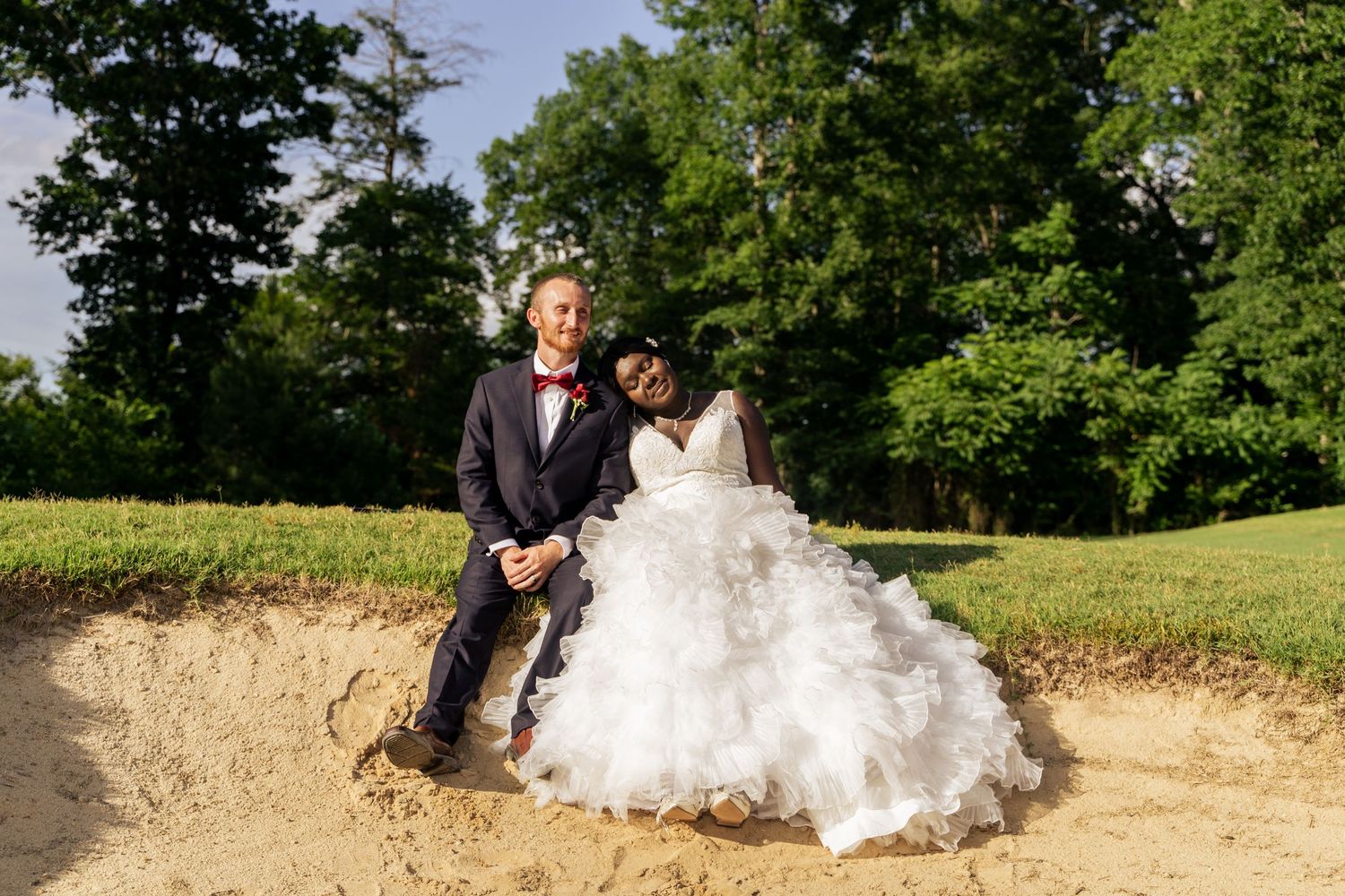 Newlywed couple married on a golf course smile for the camera tilted into each other.