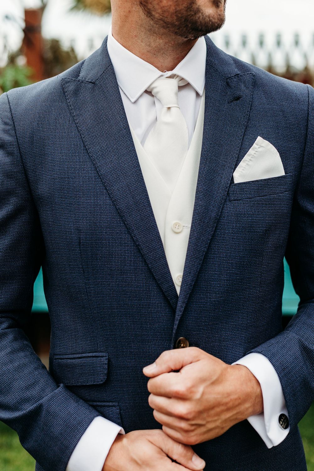 Close-up of a navy textured suit jacket with white pocket square and tie.