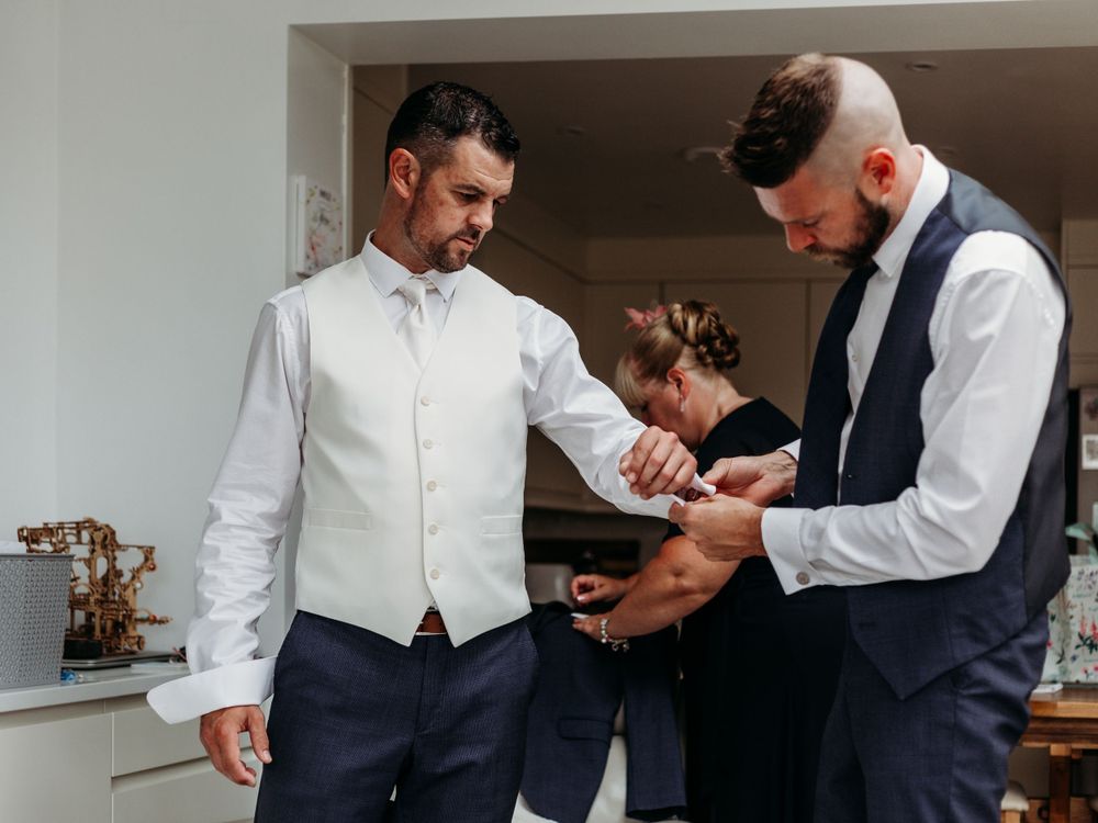 Two people in formal attire help each other with wedding day preparations.