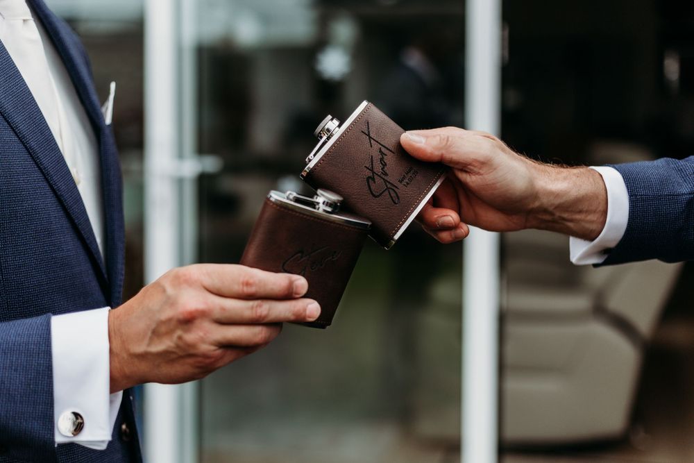 Two hands exchanging a brown leather wallet during wedding preparations.
