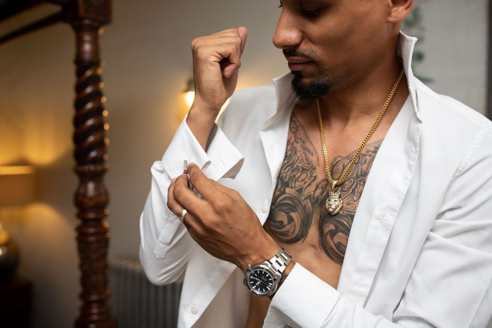 Person in white shirt with tattoos and jewelry adjusting cufflinks.