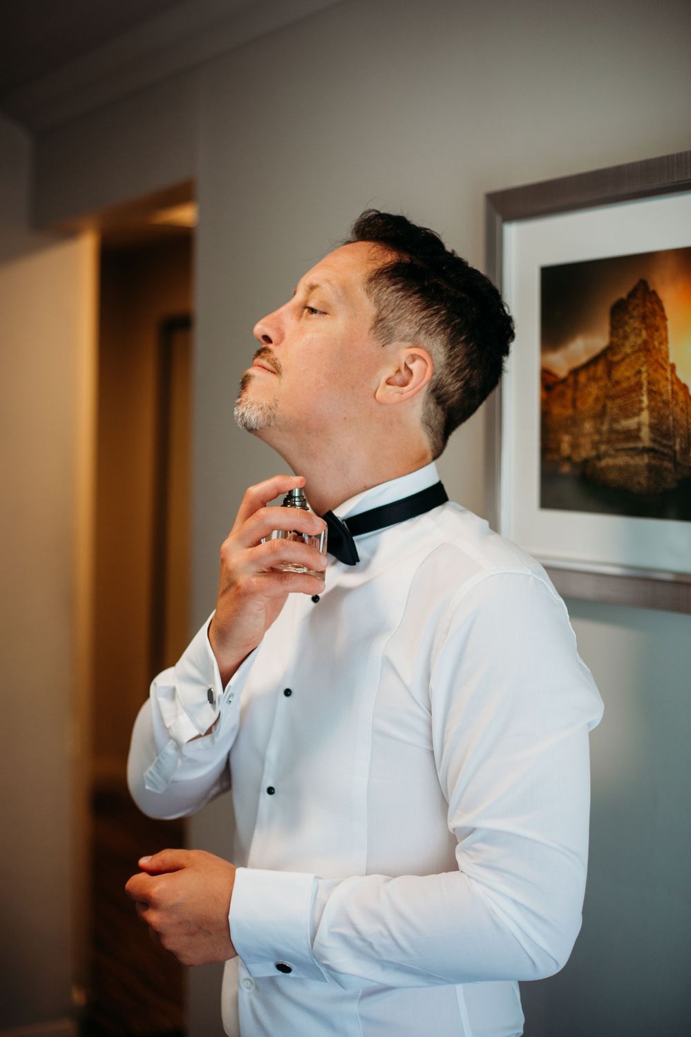 A person in white dress shirt and bow tie adjusts their collar while getting ready.