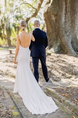 Elegant wedding couple walking along stone path under moss-draped trees.
