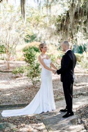 Wedding couple stands on stone path surrounded by Spanish moss draped trees.