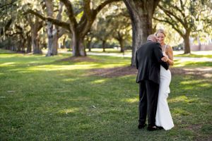 An intimate wedding moment captured on a sunlit lawn surrounded by towering oak trees.