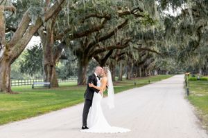 A wedding couple embraces on a tree-lined path with Spanish moss hanging overhead.