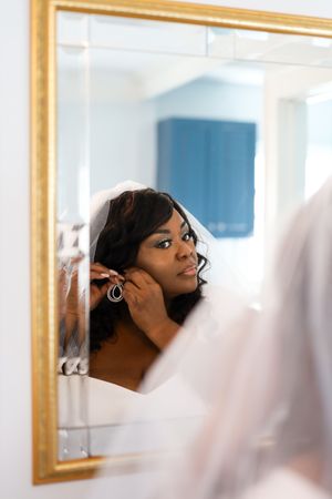 A person putting on earrings while looking in a gold-framed mirror.