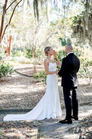 Intimate wedding moment captured in sunlit garden with Spanish moss overhead.