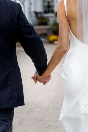 Close-up of couple holding hands in wedding attire against brick backdrop.