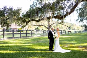 A wedding couple poses under majestic oak trees draped with Spanish moss in a picturesque garden setting.