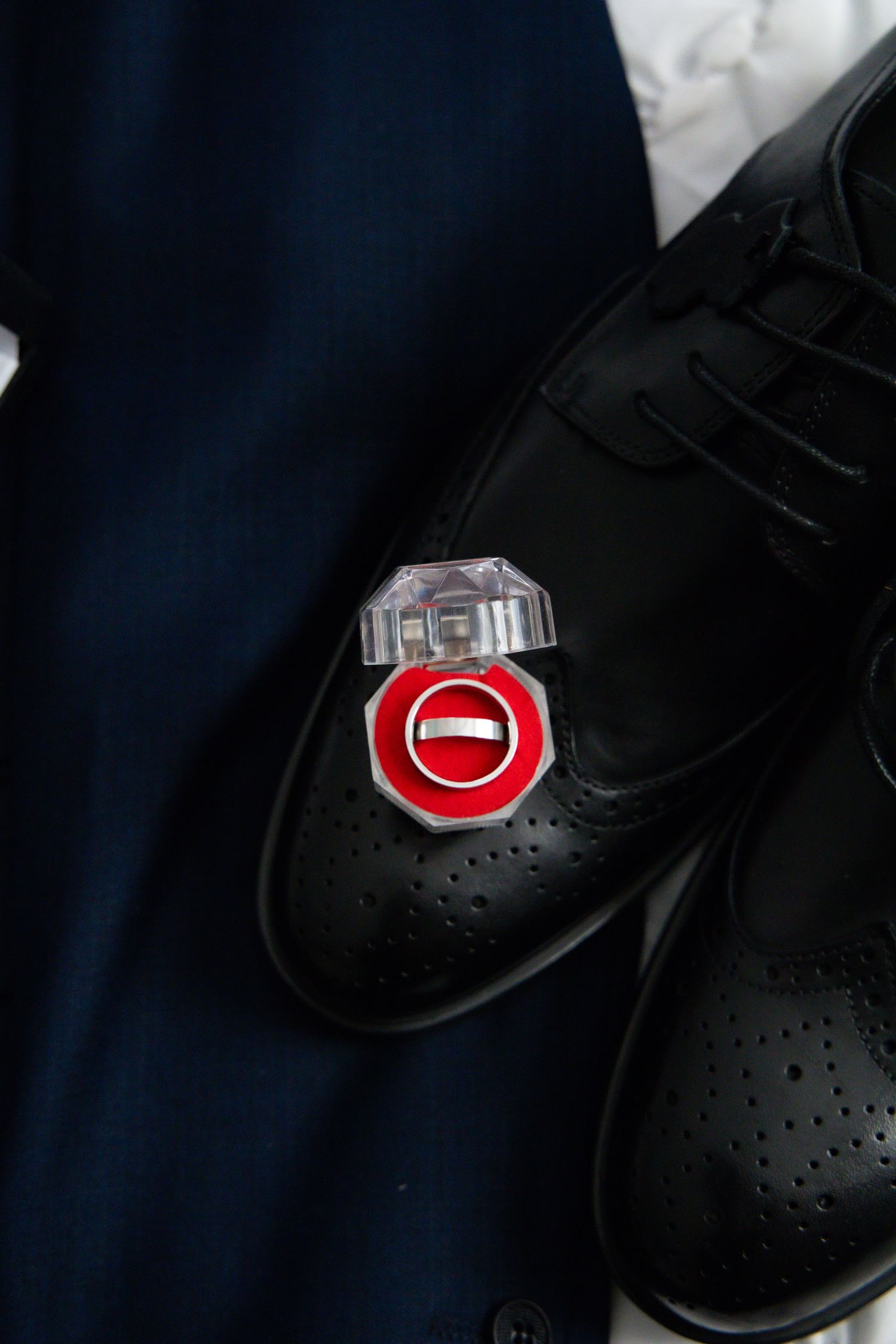 A black leather dress shoe with a wedding ring pin on it.