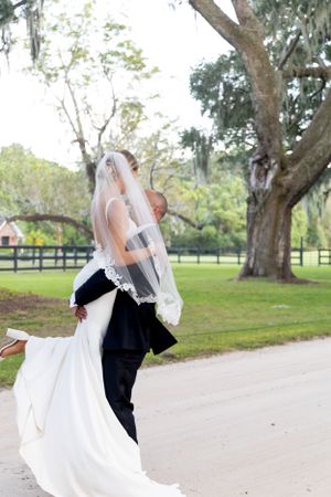 Romantic dance dip on a tree-lined path with flowing white wedding dress and veil.