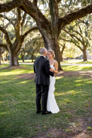 A tender wedding embrace beneath ancient oak trees draped with Spanish moss.