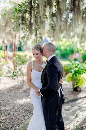Tender wedding moment shared under canopy of Spanish moss in garden setting.