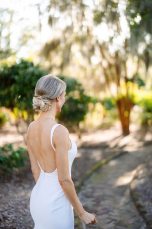 Elegant backless white wedding dress shown against lush garden backdrop.