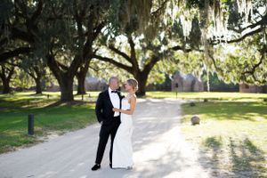 A romantic wedding photo on a path beneath Spanish moss-draped trees in golden sunlight.