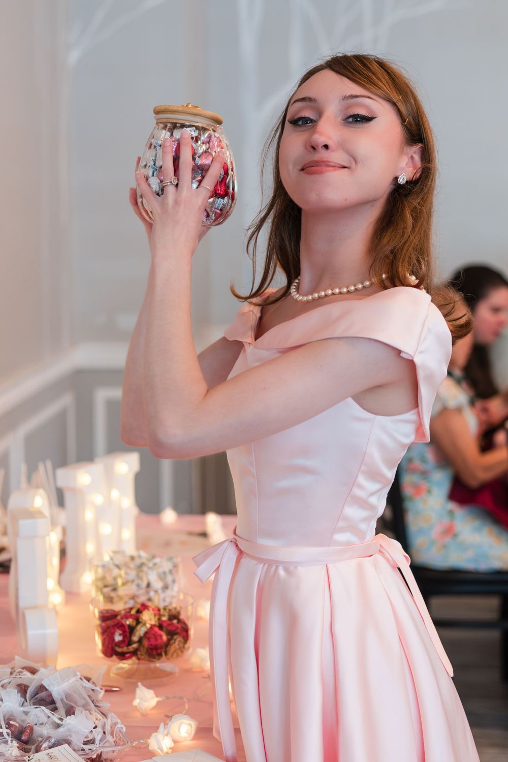 Woman in pink dress holding decorative jar at elegant candlelit table setting.