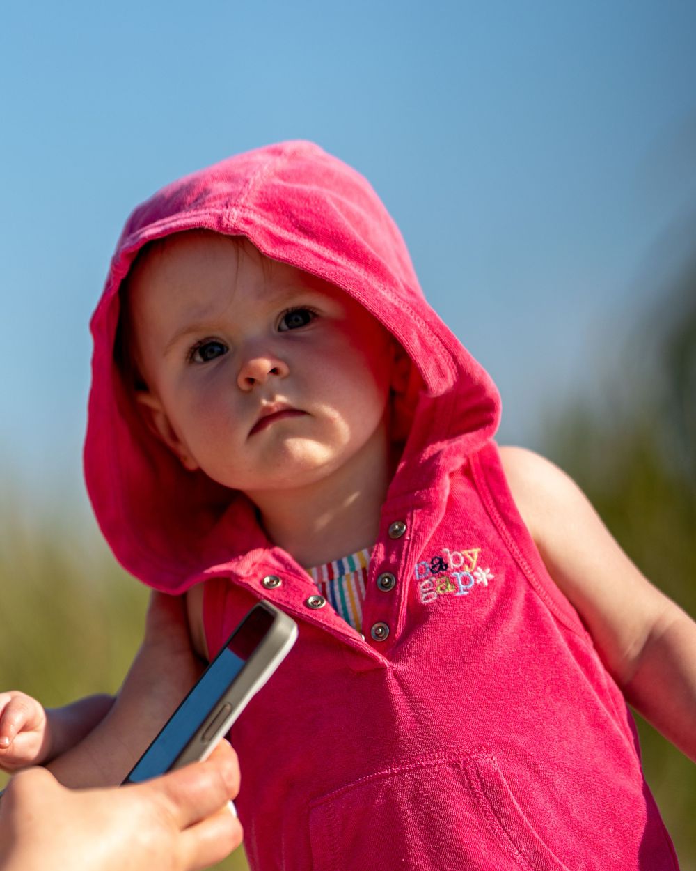 Baby wearing pink hooded outfit against blue sky background.
