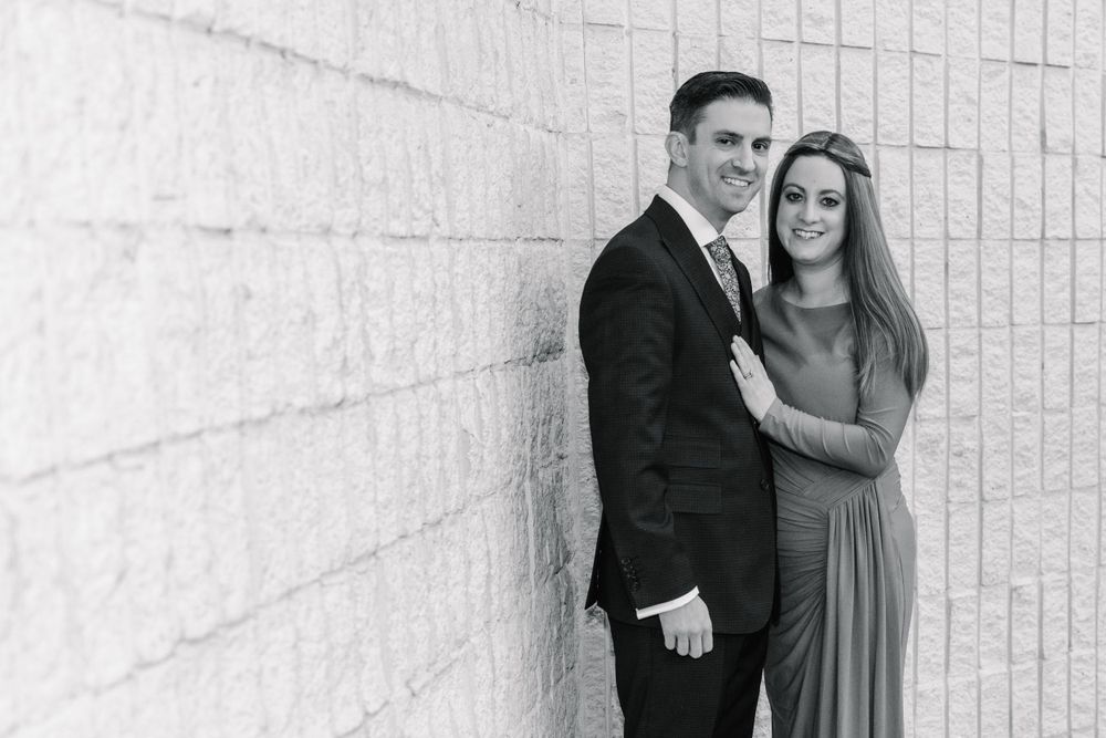 Formal couple poses against white textured wall in black and white photography.