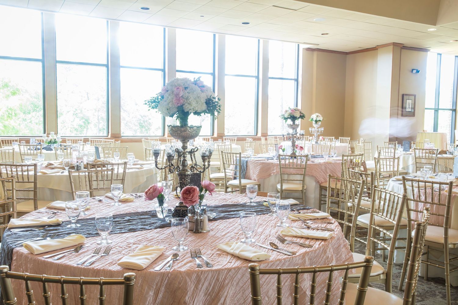 Spacious banquet hall set with round tables and gold chiavari chairs for an elegant wedding reception.