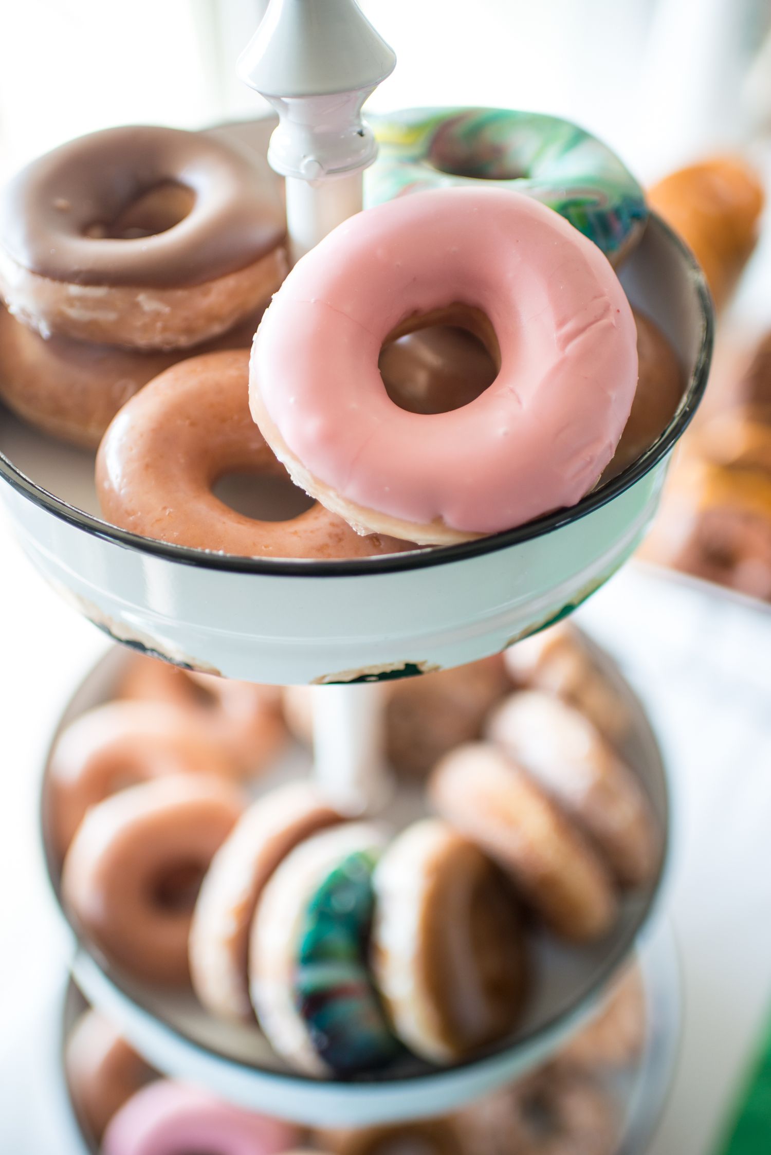 Colorful glazed donuts displayed on a white tiered serving stand.