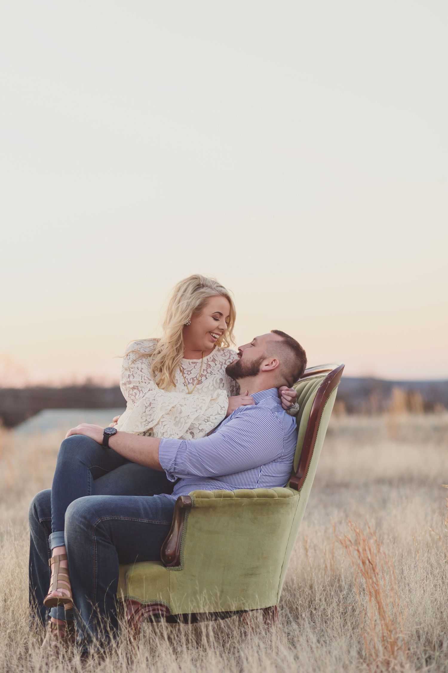 Couple sharing intimate moment on vintage chair in golden field at sunset.