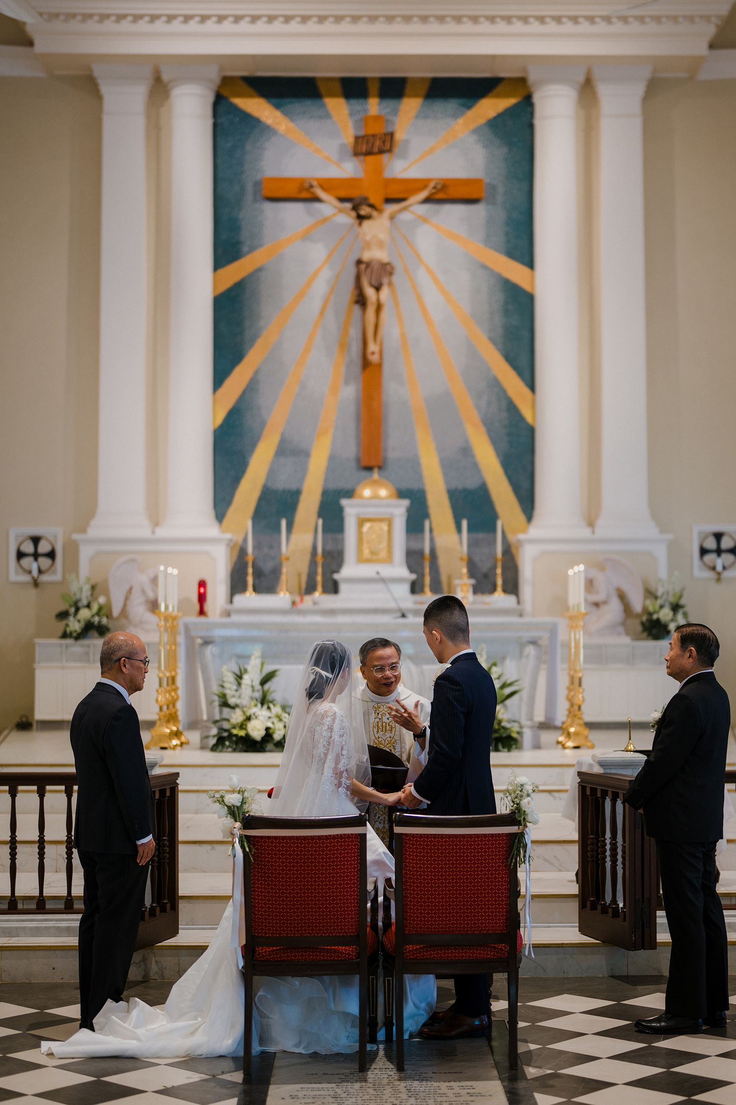 Wedding ceremony taking place at church altar with distinctive sunburst crucifix backdrop.
