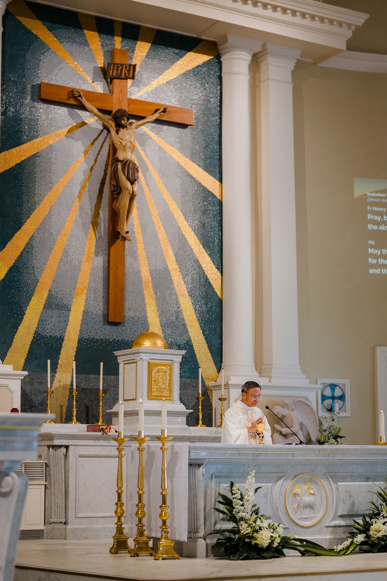 Close-up of church altar showing wooden crucifix against blue and gold sunburst mosaic background.