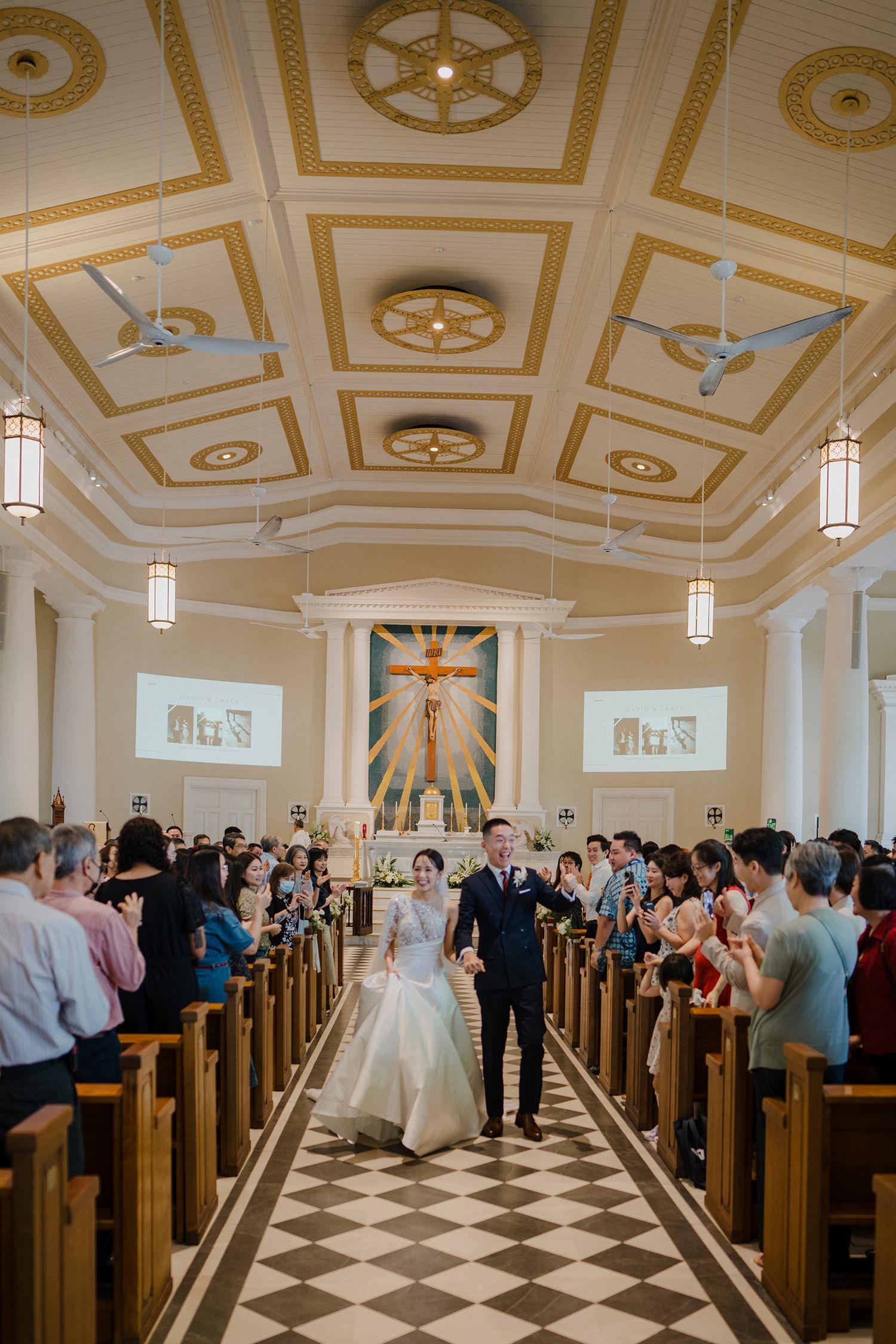 Wide view of a church wedding ceremony showing guests seated in wooden pews under an ornate ceiling.