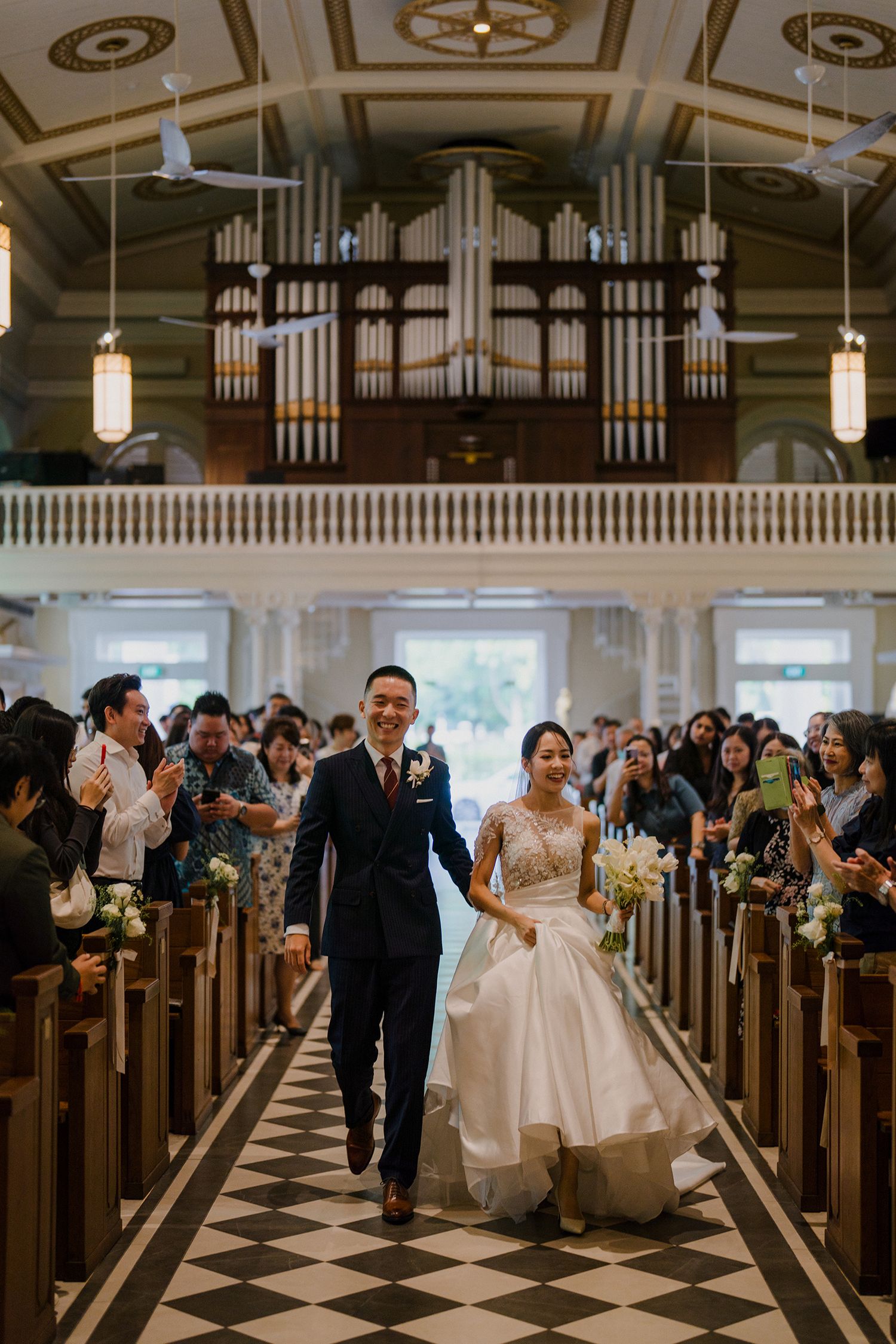 Wedding ceremony in a grand church with ornate organ pipes and checkered floor.