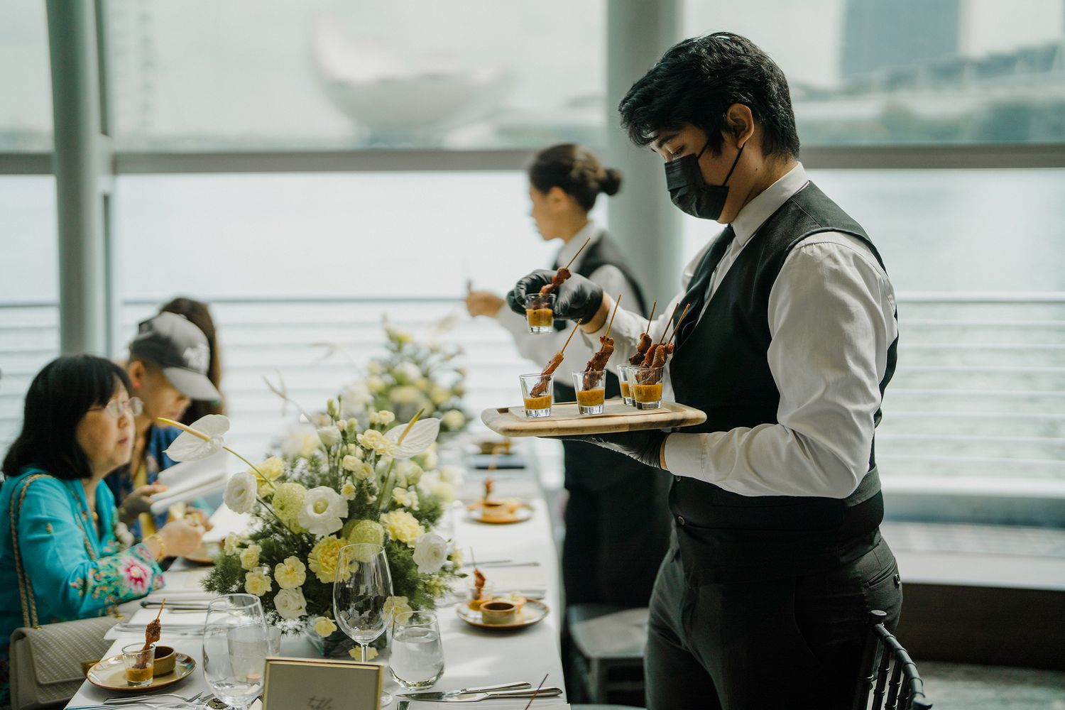 Modern wedding reception venue with guests dining near large windows.