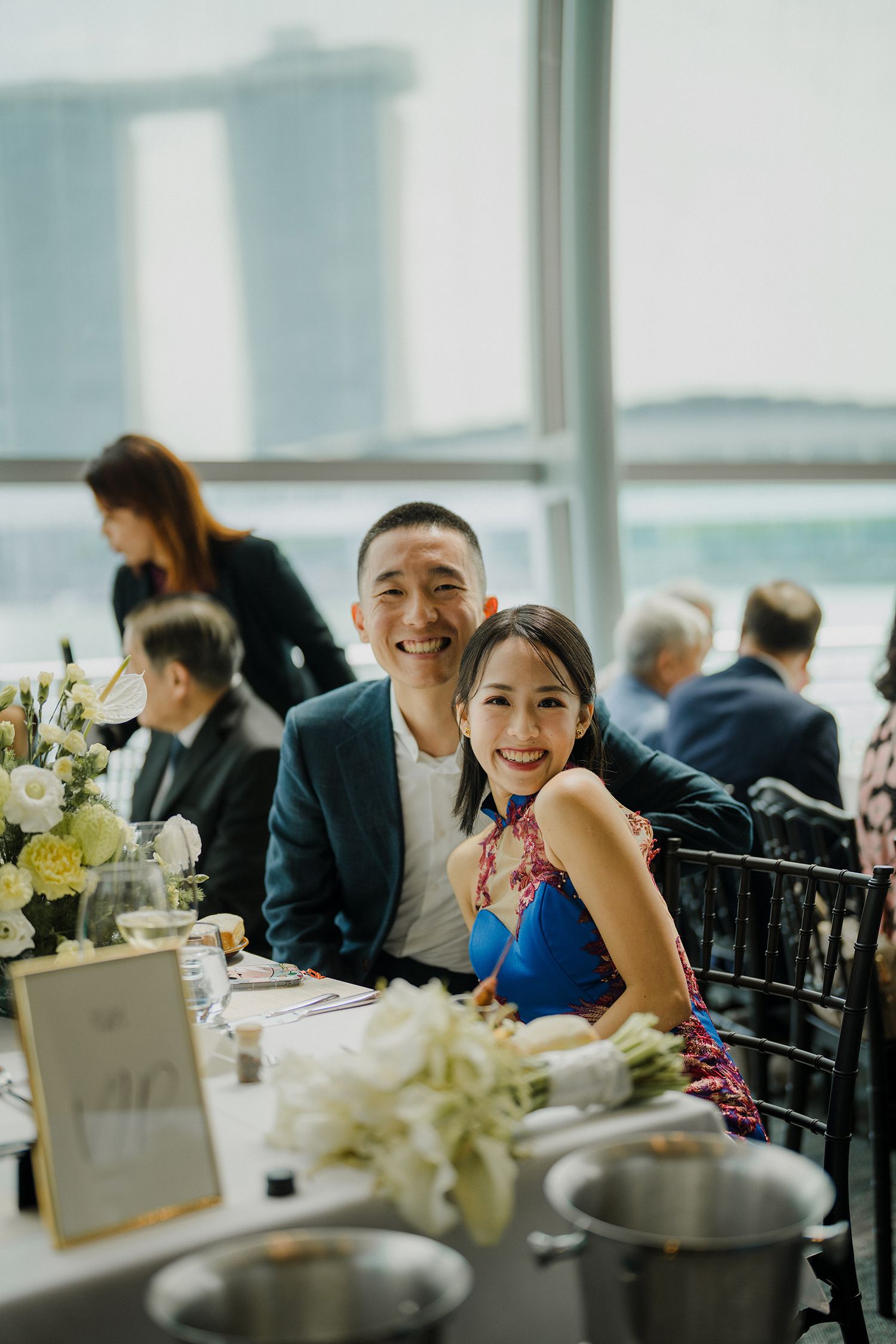 Wedding reception dining room with elegant table settings and city views through large windows.