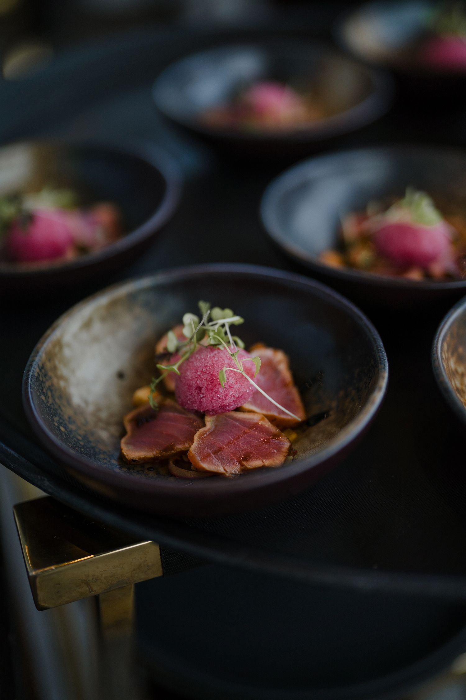 Seared tuna dish presented on dark plates with pink center and garnish.