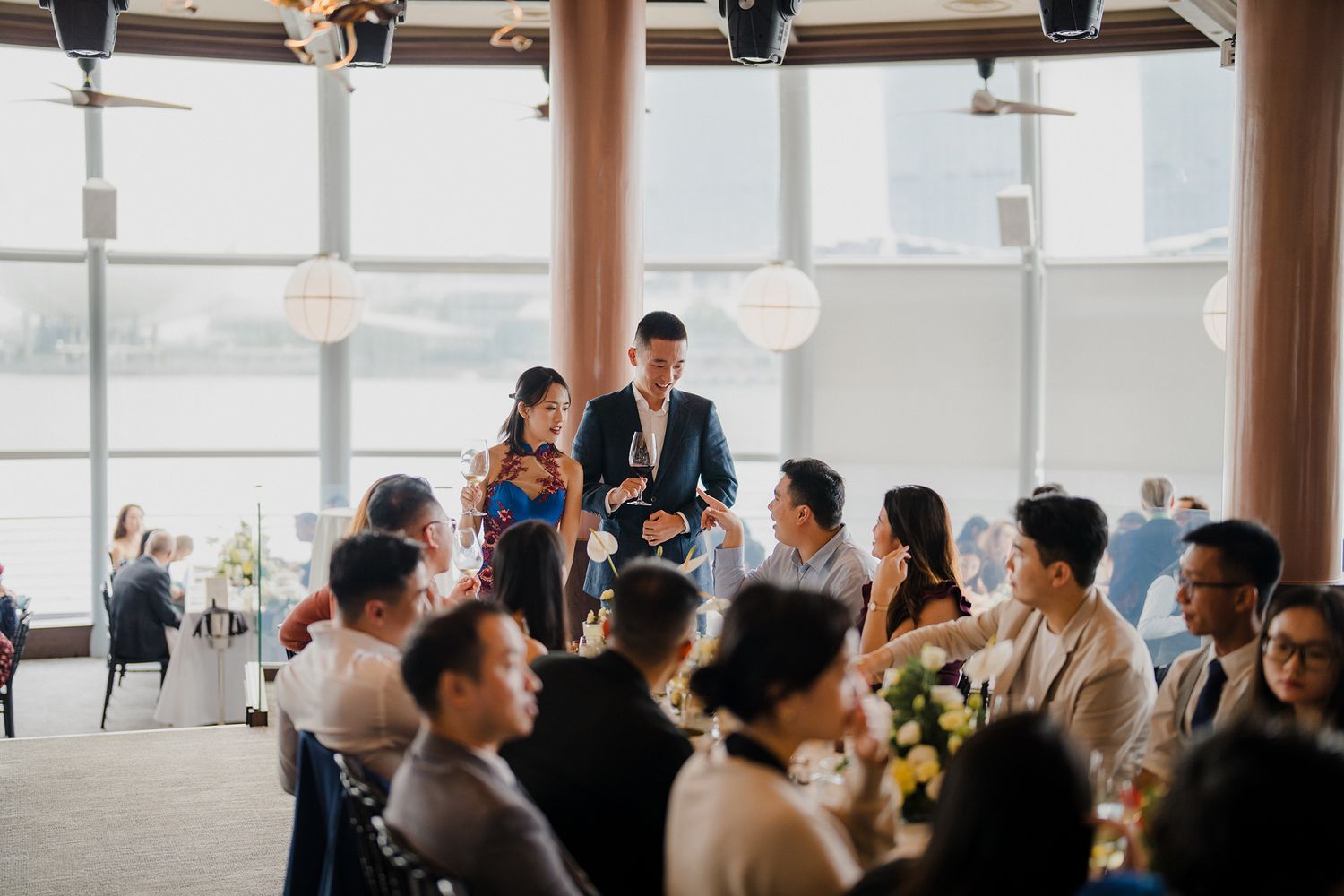 Elegant wedding reception in a bright venue with white floral centerpieces and formal table settings.