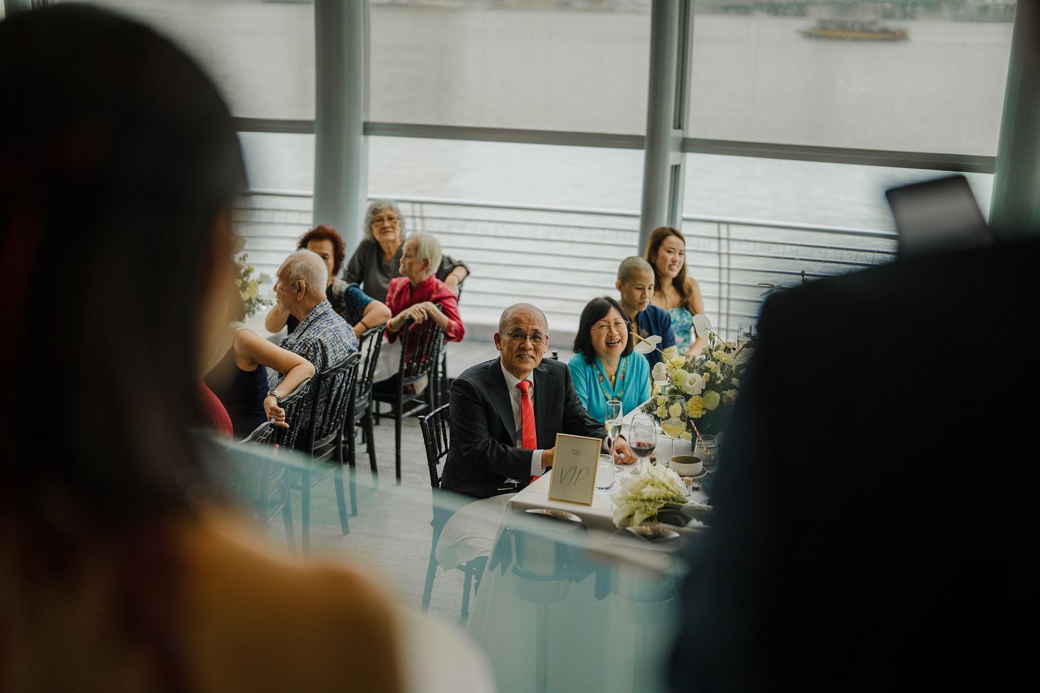 Waterfront venue with guests seated at tables decorated with blue and white floral arrangements.
