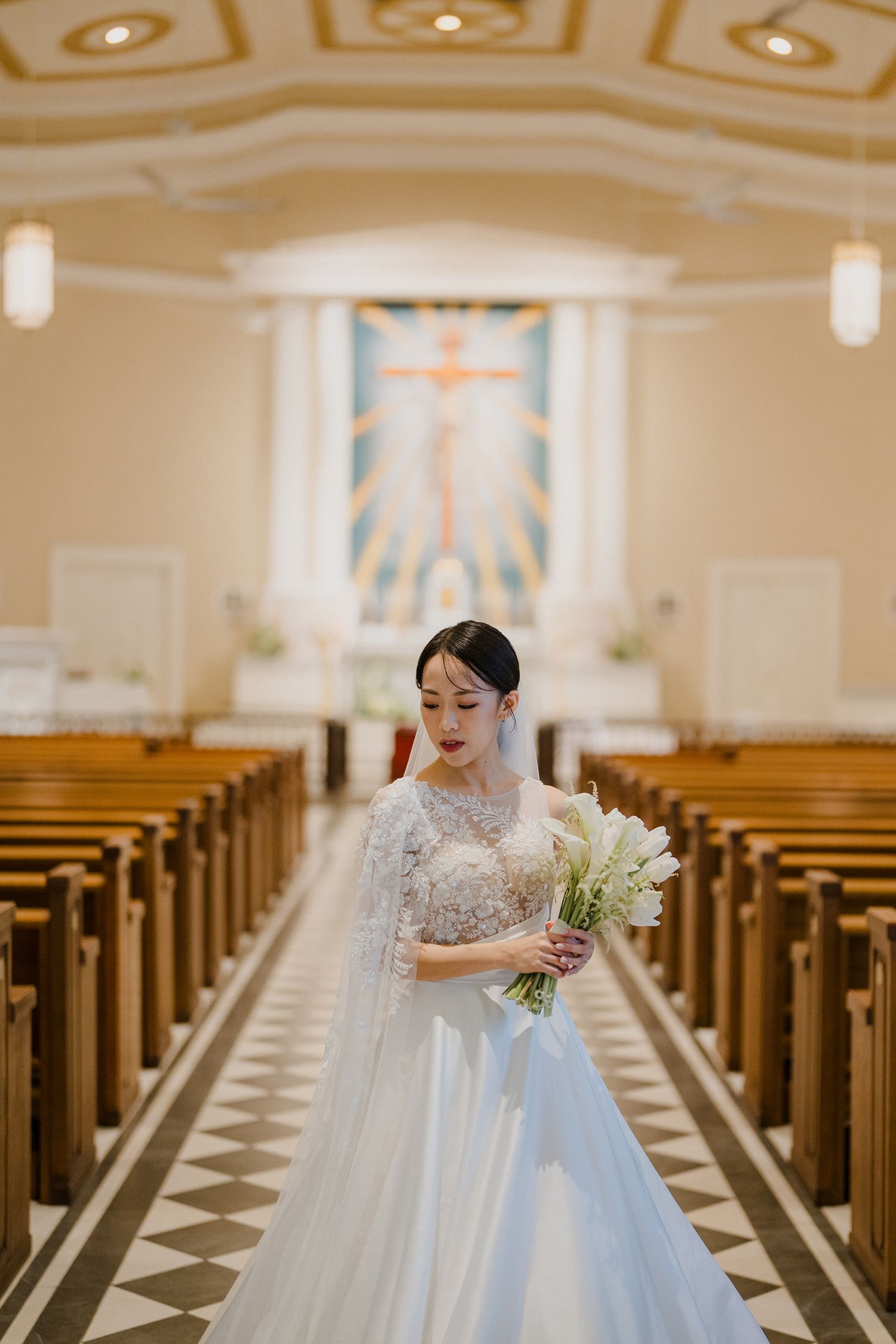 A bride in a white ballgown walks through an elegant church with checkered floors and ornate decor.