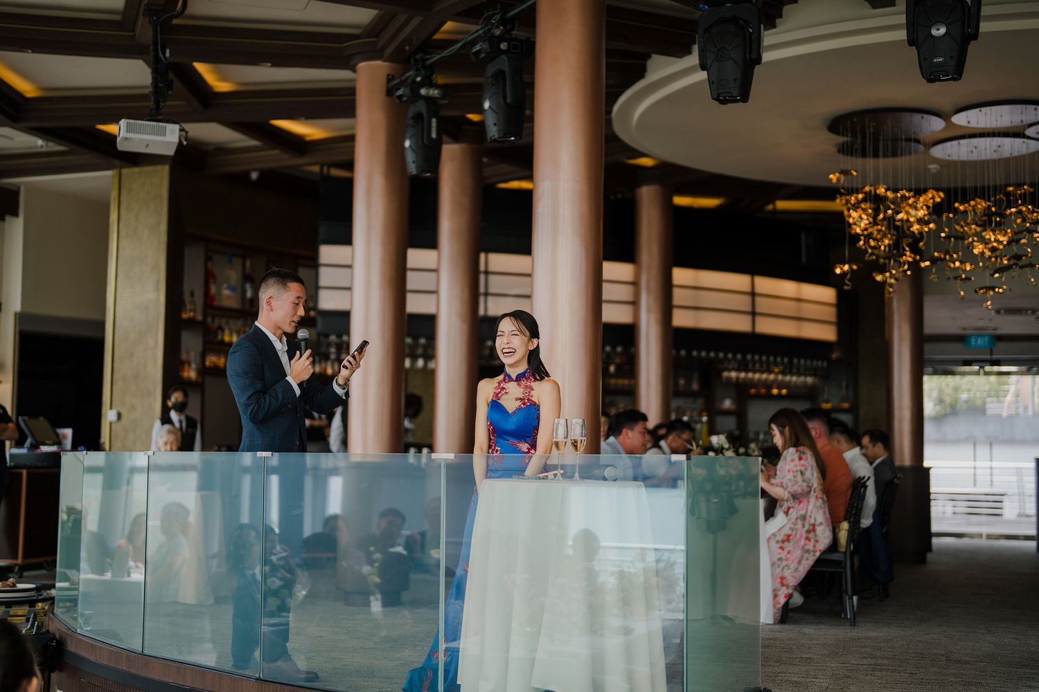 Formal event at a modern venue with glass railings and decorative lighting fixtures overhead.
