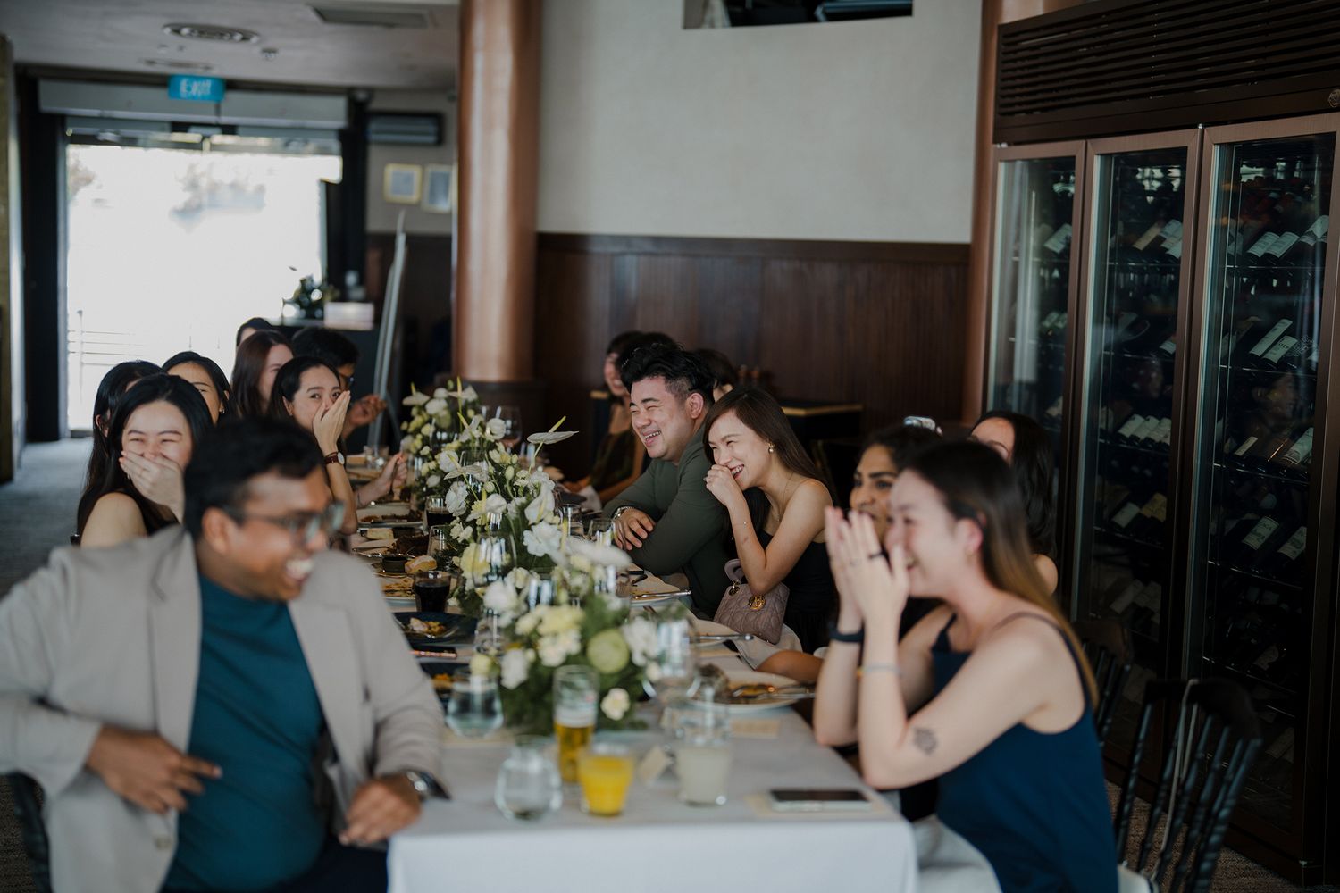 Wedding reception guests seated at long tables decorated with white floral arrangements and glassware.