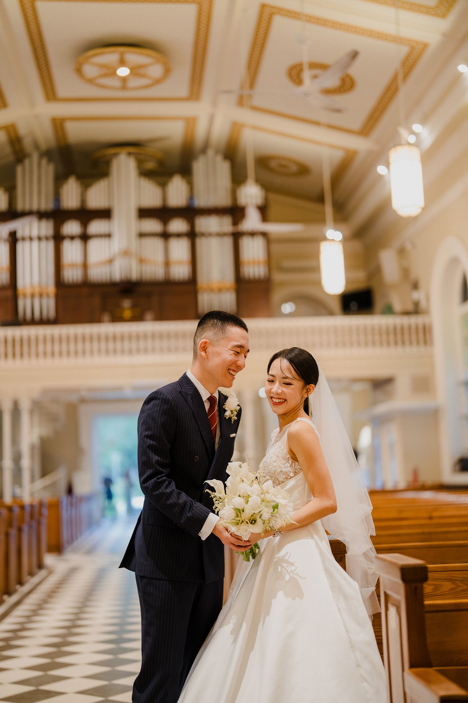 Newlyweds share joyful moment in church with checkered floor and ornate ceiling.
