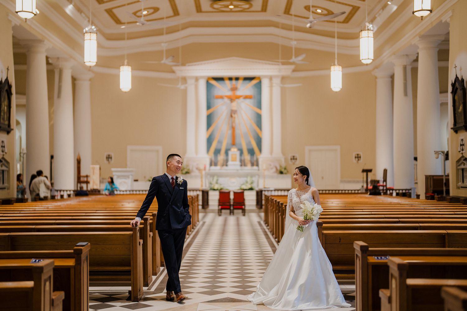 Elegant church wedding ceremony in a grand cathedral with checkered floor and hanging pendant lights.